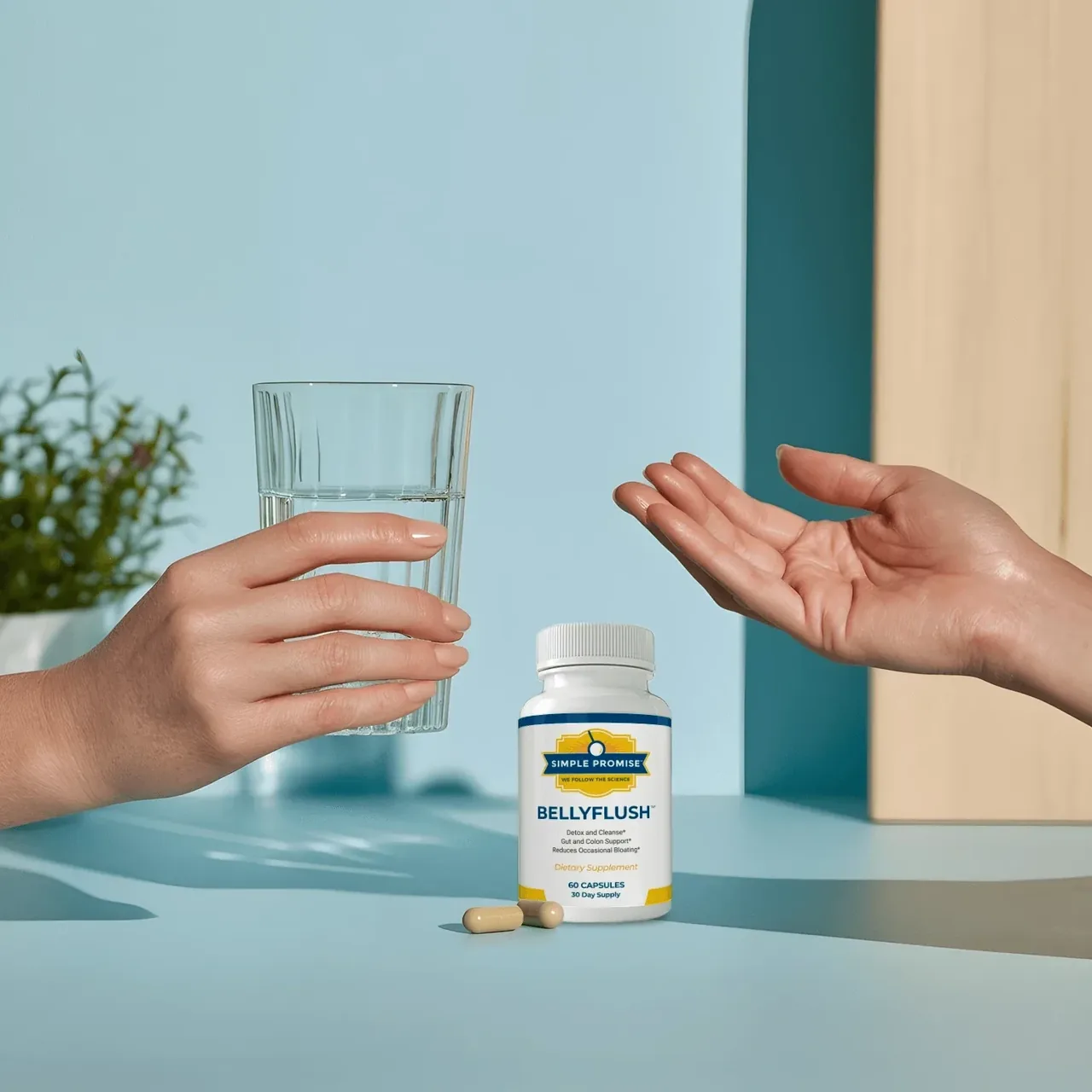 Two hands, a glass of water and two BellyFlush capsules on a table